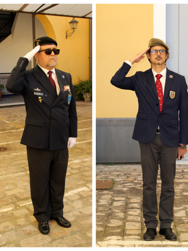 Dos hombres saludando con uniformes militares y civil en una plaza histórica.