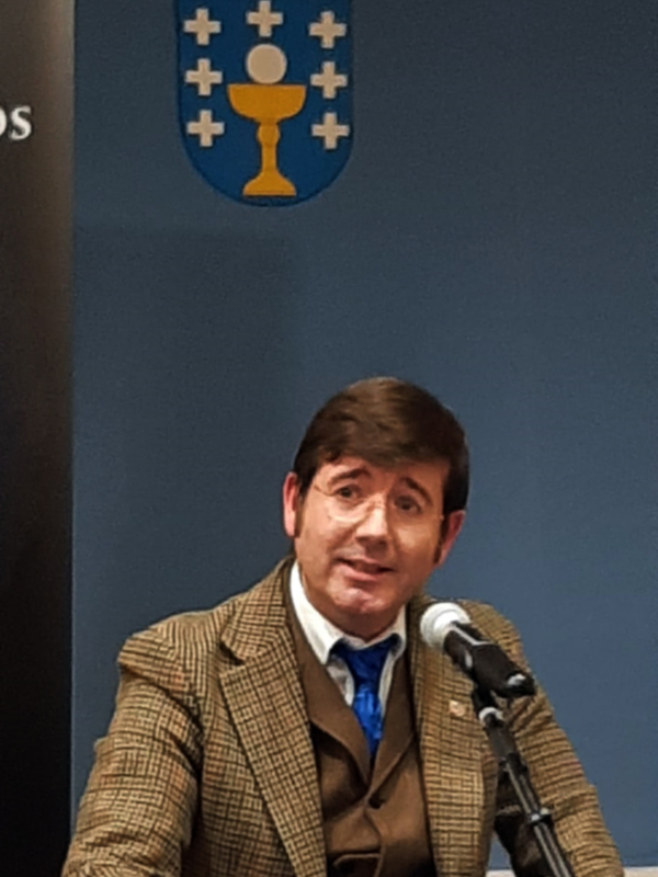 Hombre hablando en una conferencia de prensa con un escudo en el fondo.