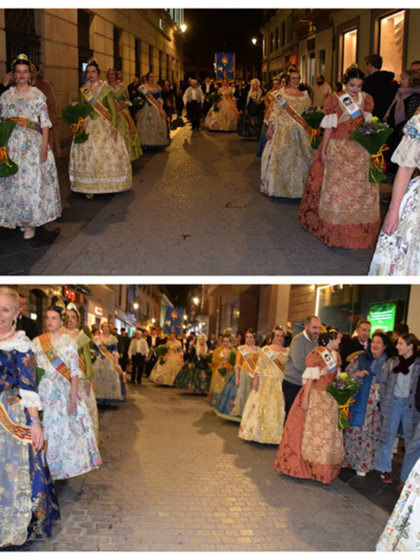 Desfile de falleras desfilando por una calle iluminada, vestidas con trajes tradicionales y sashes.