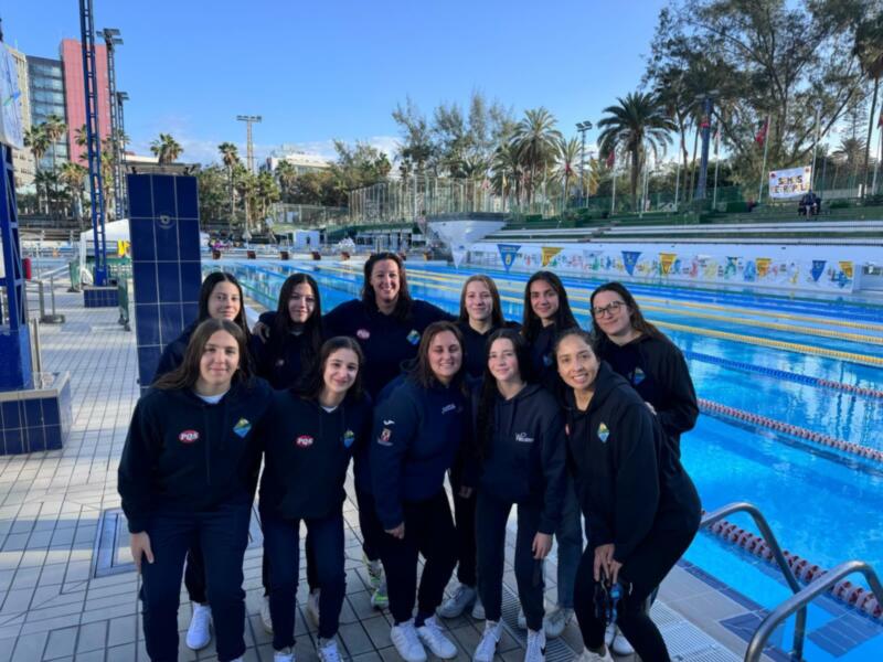 Equipo de natación femenino posando junto a una piscina al aire libre.