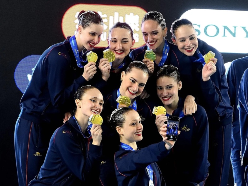 Equipo español de natación sincronizada celebrando con medallas de oro en un podio.