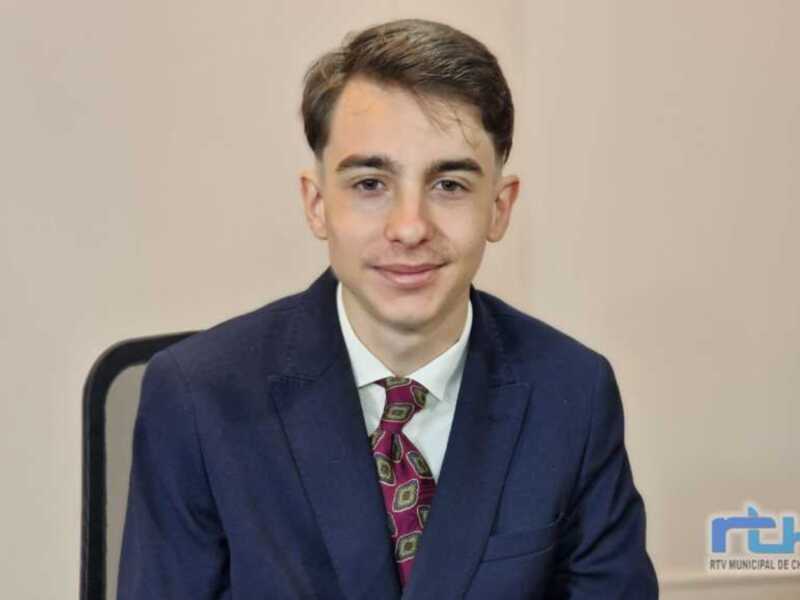 Joven en traje y corbata, sentado en una silla, en un entorno profesional.