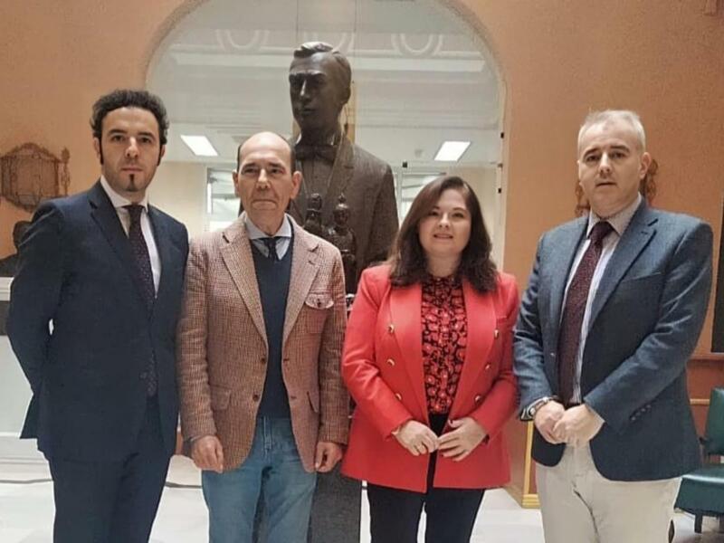 Cuatro personas posan frente a una estatua en un interior clásico.
