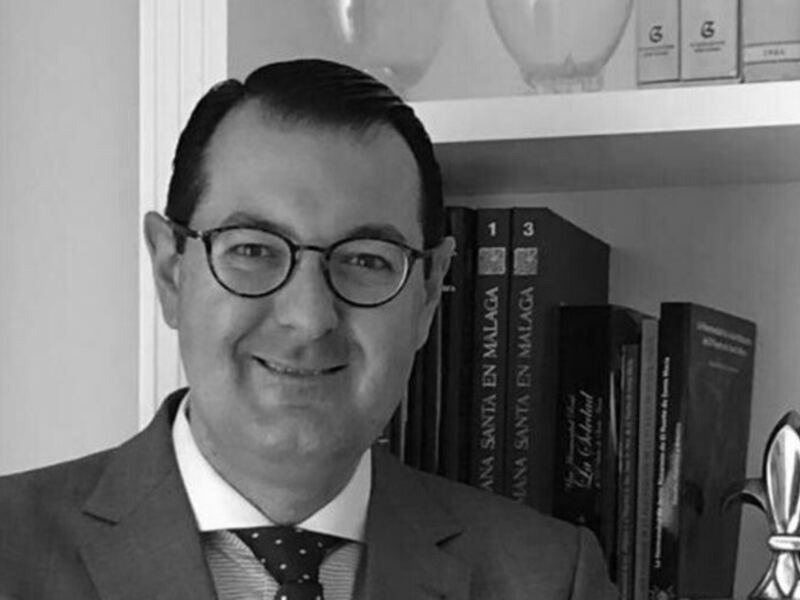 Un hombre en traje y corbata, posando frente a una estantería llena de libros, en una imagen en blanco y negro.