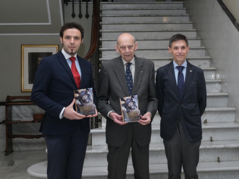 Tres hombres en trajes sostienen libros titulados 'Relato Médico de la Pasión Segundo San Juan' en un ambiente formal.