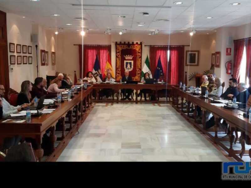Reunión de trabajo en una sala de conferencias con banderas y escudo municipal en el fondo.