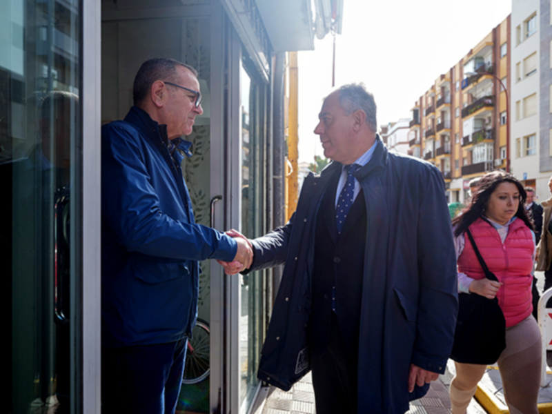 Dos hombres saludándose en una calle urbana, con edificios de apartamentos al fondo.
