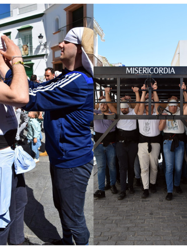 Desfile con personas con banderas y una persona con una bandera en la cabeza en una calle con edificios blancos y azules en el fondo.