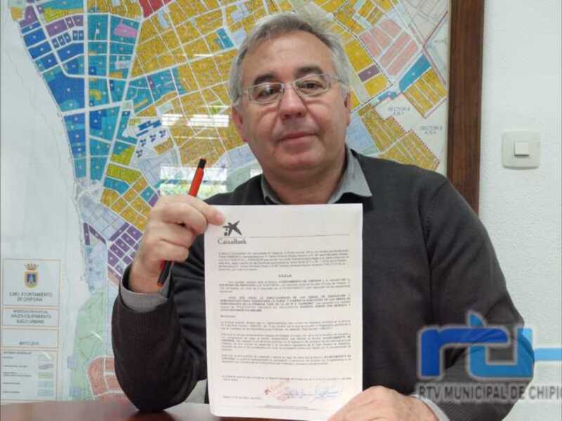 Persona sosteniendo un documento frente a un mapa y el escudo del Ayuntamiento de Chipiona.