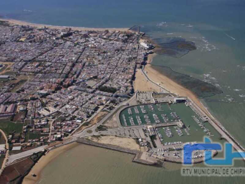 Vista aérea de Chipiona, con la ciudad, la playa y el puerto marítimo en primer plano.