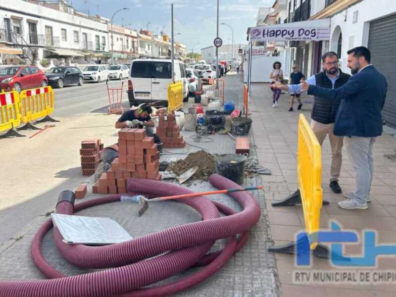 Trabajos de mantenimiento en la calle, con personas trabajando y maquinaria en el suelo. Se puede ver una señal de tráfico y una estructura de hormigón en el fondo.