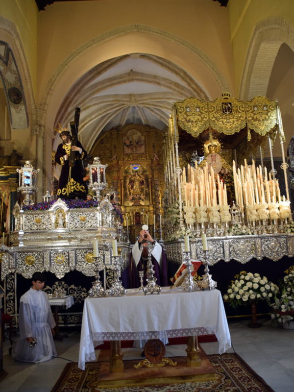 Interior de una iglesia con altares ornamentados y velas, representando una procesión religiosa.