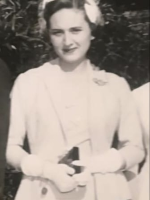 Una mujer en un traje blanco de los años 50, posando con una corona y un ramo en la mano.