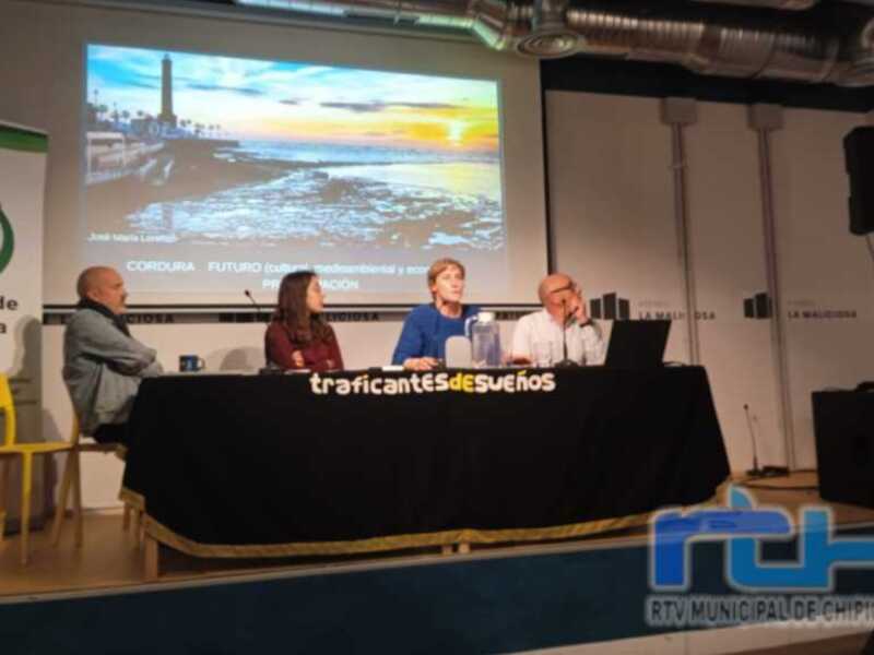Panel de discusión sobre el futuro cultural, medioambiental y económico en Chipiona, con proyección de una imagen del Faro de Málaga al atardecer.