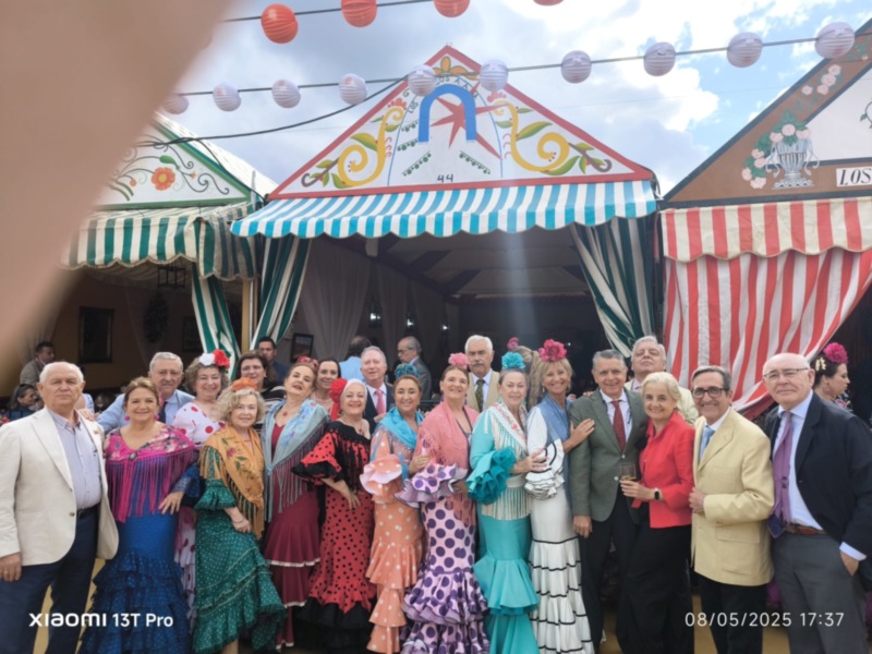 Fiesta tradicional con personas vestidas con trajes de flamenca y trajes formales en un evento celebrado bajo carpas decoradas.