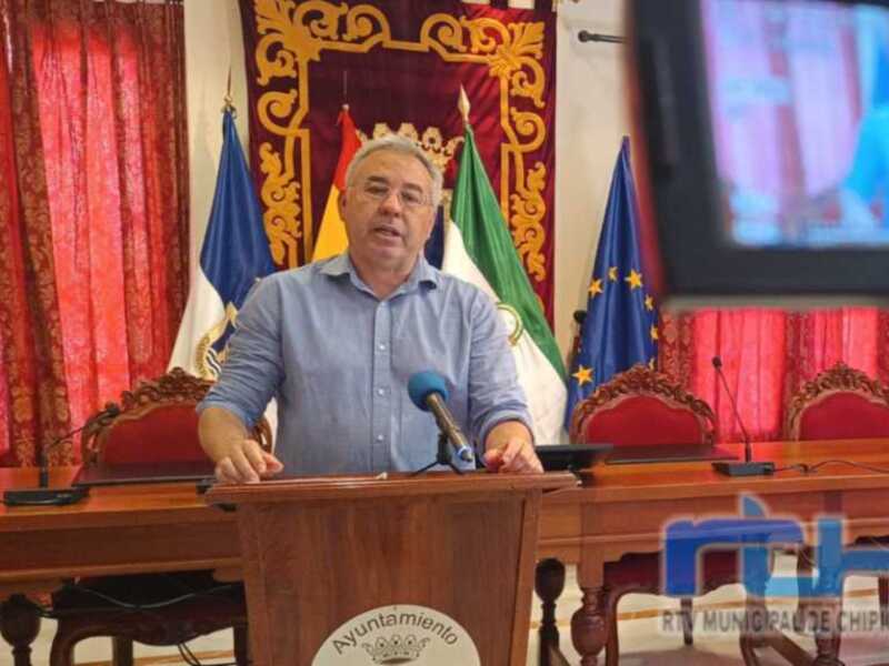 Persona hablando en un podio del Ayuntamiento de Chipiona, con banderas y un escudo en el fondo.