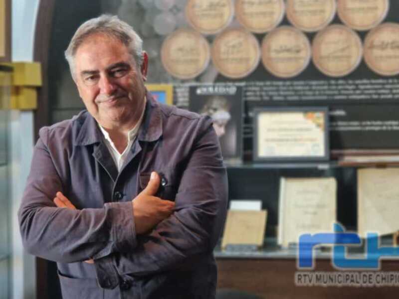 Retrato de hombre con brazos cruzados, fondo con placas y certificados.