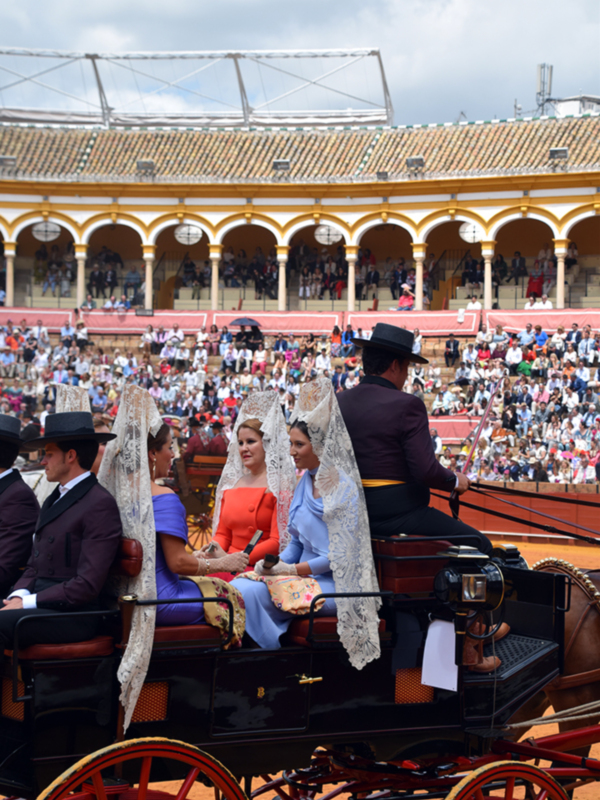 Fiesta en la plaza de toros con carruaje y damas vestidas con mantillas tradicionales.