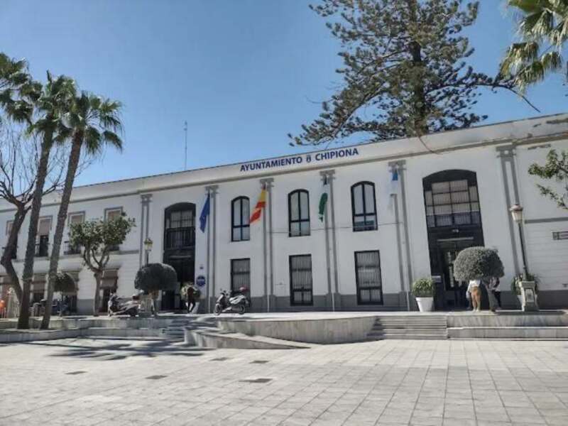 Ayuntamiento de Chipiona, edificio municipal con banderas y plaza frente a él.