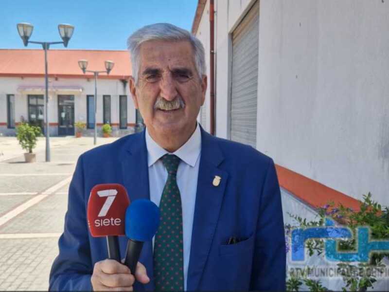 Entrevista en vivo con un hombre en traje azul y corbata, sosteniendo micrófonos de RTV Municipal de Chipiona.