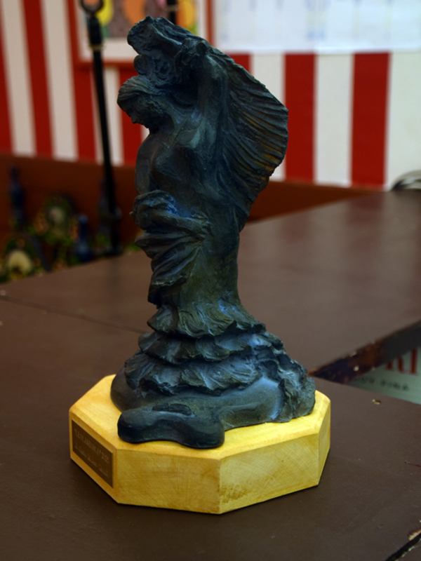 Sculpture of a figure with wings, displayed on a wooden base.