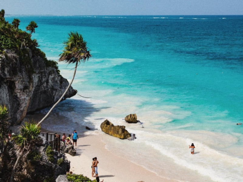 Playa del Carmen, México: una vista panorámica de la costa con acantilados, palmeras y turistas disfrutando de la arena blanca y el agua turquesa.