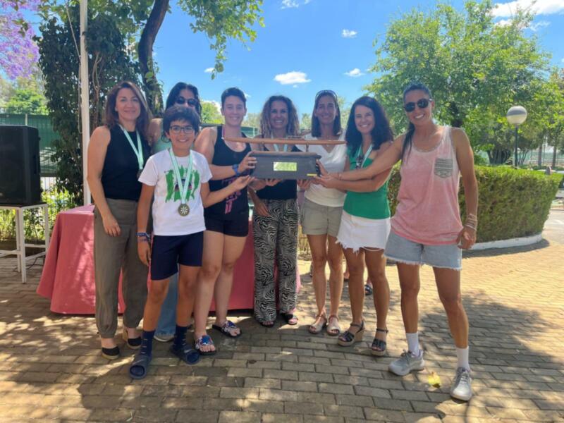 Equipo ganador celebrando con un trofeo en un evento al aire libre bajo un árbol.