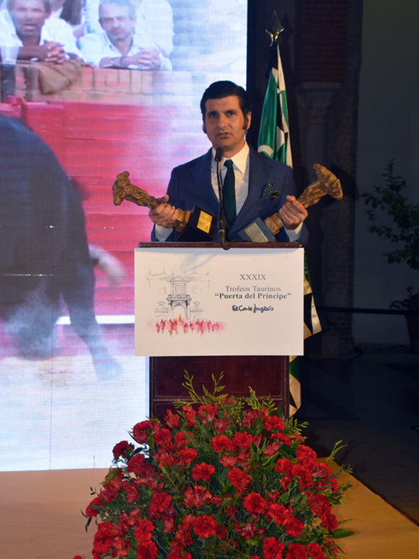 Hombre en traje recibiendo trofeos en ceremonia taurina 'Puerta del Príncipe'.