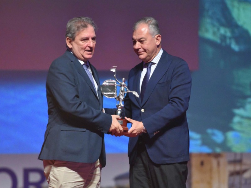 Entrega de un premio en un evento formal en un escenario iluminado.