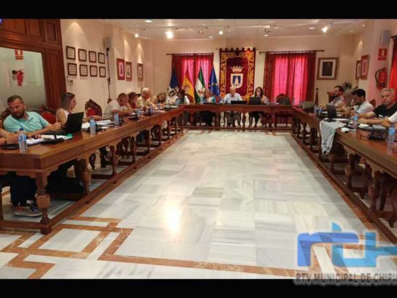 Reunión de consejo municipal en una sala elegante con mesas y sillas alrededor.