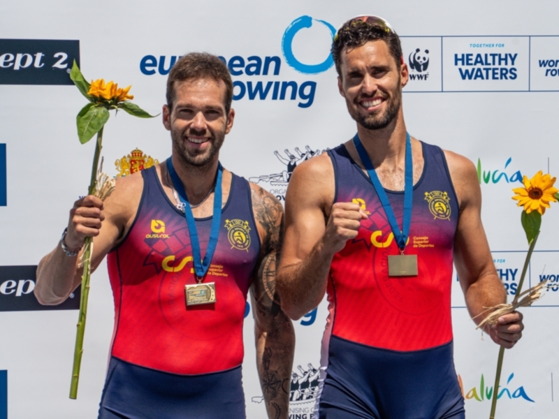 Medallistas de remo celebrando en el podio con flores y medallas.