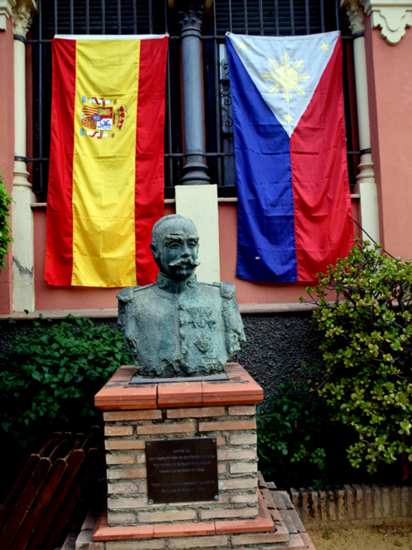 Busto de militar frente a banderas de España y Filipinas, representando la presencia colonial española en el país.