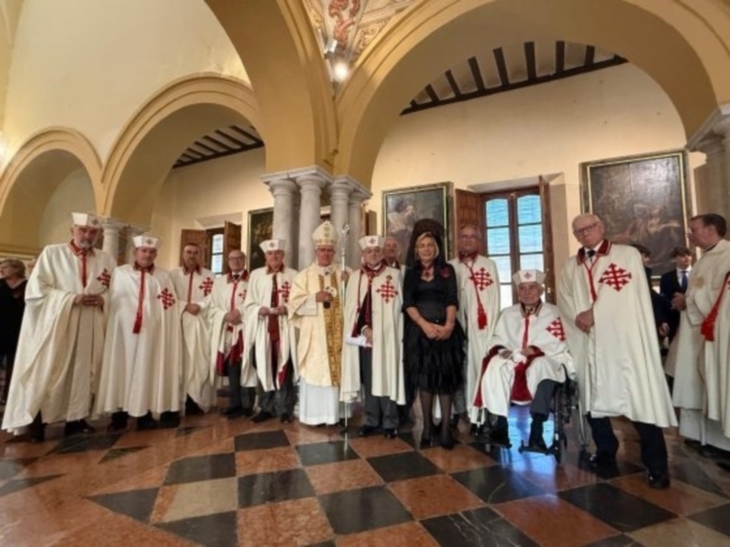Celebración religiosa en un interior con arcos y altares, con personas vestidas con túnicas blancas y un sacerdote en el centro.