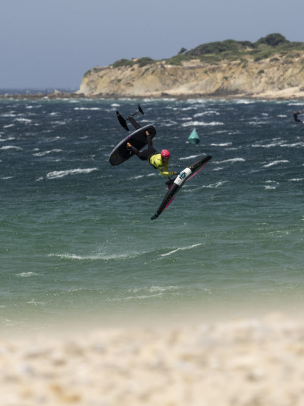 Windsurfer performing a dramatic jump over the ocean, with cliffs and a clear sky in the background.