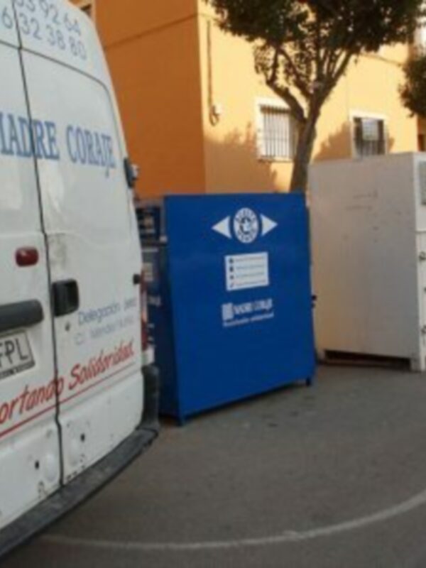 Vehículo de transporte solidario junto a contenedores de reciclaje y un panel informativo.