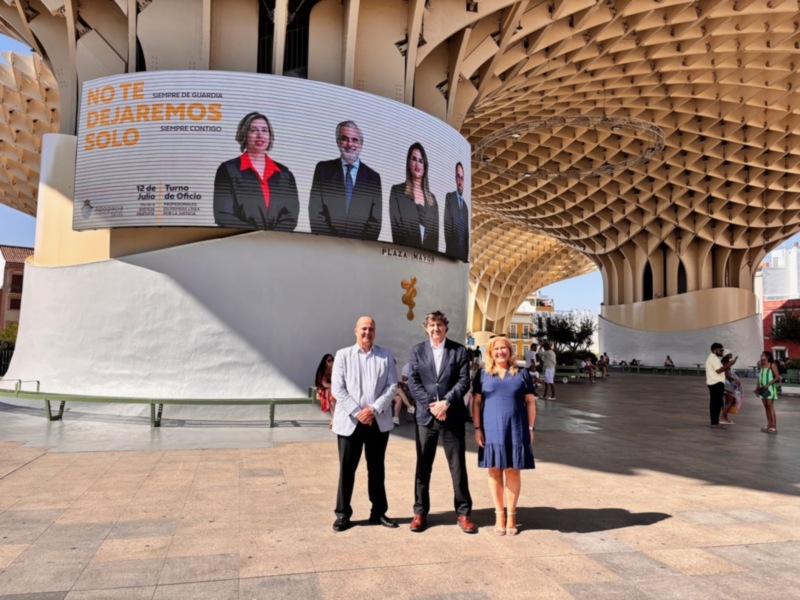 Tres personas posan frente a un mural con la frase 'No te dejaré solo' en el Metropol Parasol de Sevilla.