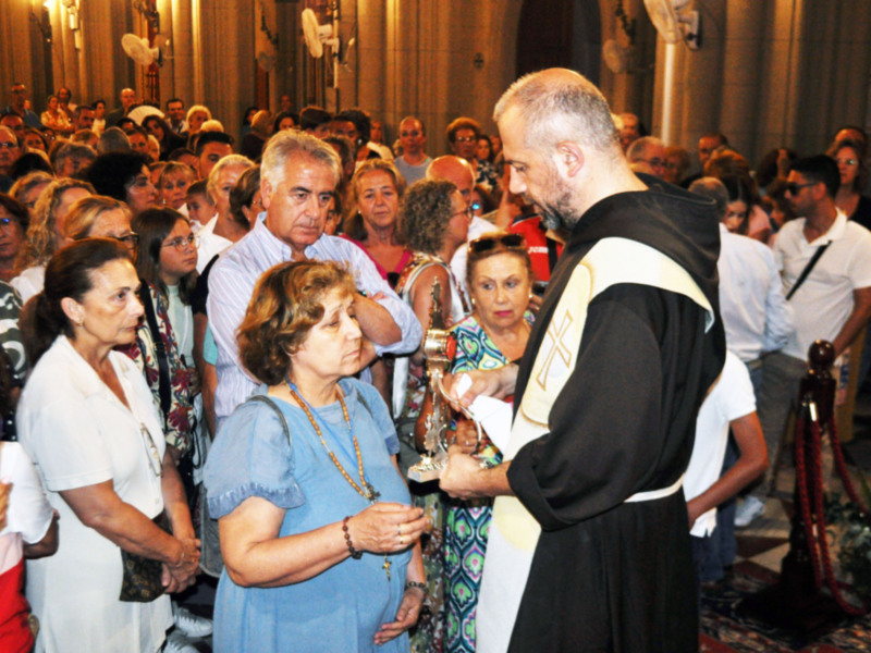 Un sacerdote bendice a una mujer en una procesión religiosa dentro de una catedral llena de fieles.