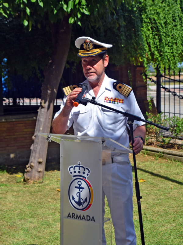 Un oficial de la Armada española pronuncia un discurso en un evento público, con un escudo de la Armada en el fondo.