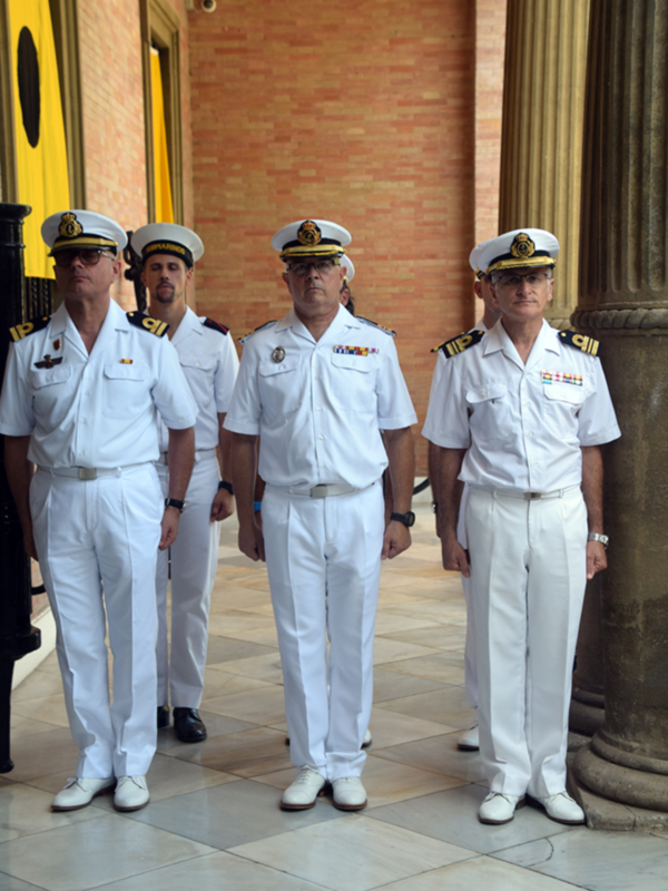 Fotografía de oficiales militares en uniforme blanco, posando en una entrada con columnas de mármol y fondo de pared de ladrillo rojo.