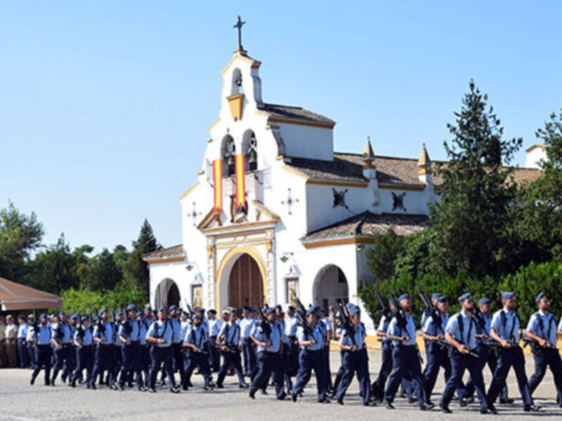 Gente en uniforme caminando en una procesión militar frente a una iglesia con una cruz en la parte superior.