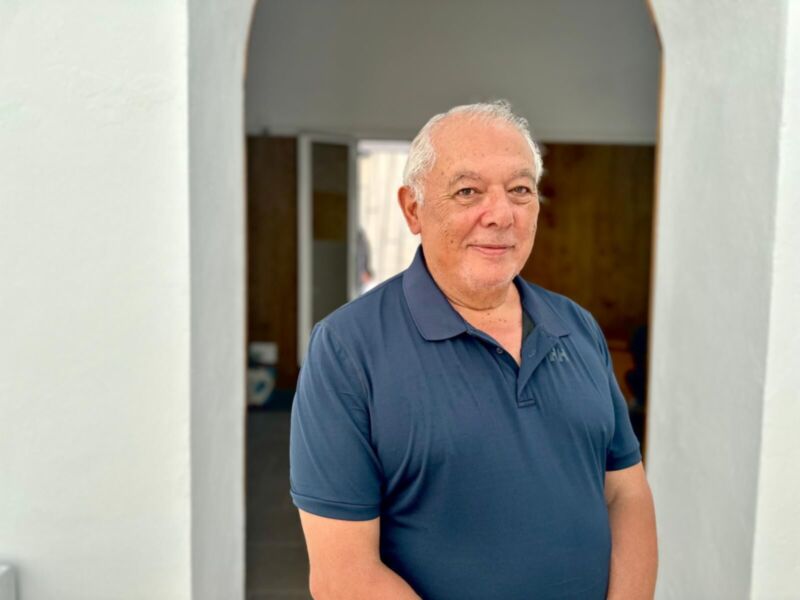 Elderly man in a blue polo shirt standing in a doorway.