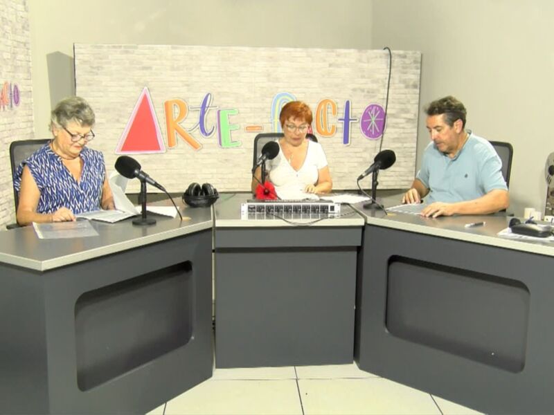 Dos personas sentadas en una mesa de estudio, con micros en frente y un fondo con la palabra 'ARTE'.