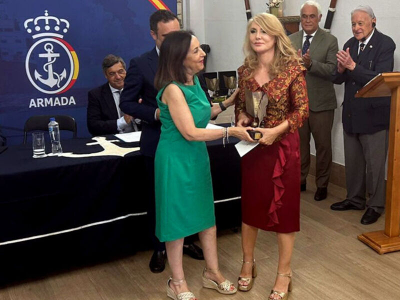 Dos mujeres sostienen un premio mientras otros individuos observan en una conferencia de prensa.