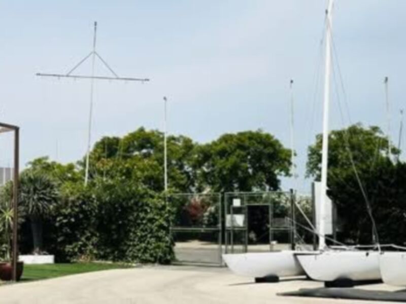 Vista de un puerto deportivo con varios veleros amarrados y un césped verde en primer plano.