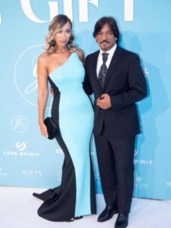 Elegante pareja posando en un evento formal, con la mujer vestida con un vestido azul claro y el hombre con una chaqueta negra y corbata negra.