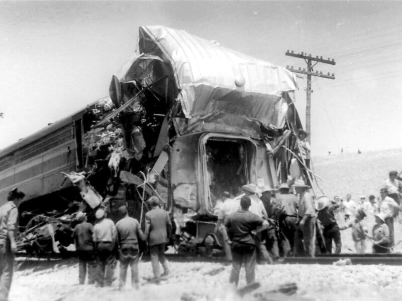 Train wreck with debris scattered and people gathered around the scene.