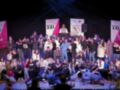 Grupo de jóvenes en una presentación en un escenario con pancartas de Barraca XXI en el fondo.
