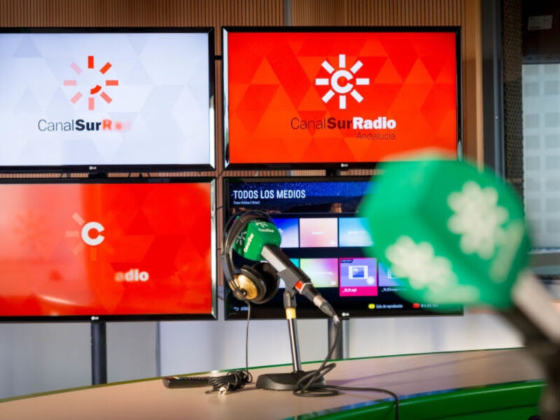 Sala de radio con televisores y micrófono en primer plano.