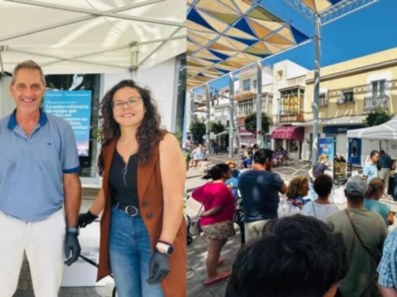 Voluntarios en un evento comunitario al aire libre en una plaza con tiendas y sombrillas.