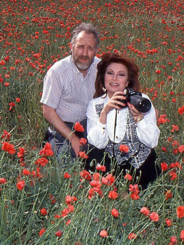 Una pareja en un campo de amapolas, la mujer toma una foto con su cámara.
